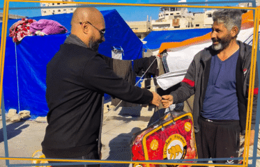 متطوع يقدّم حرامًا شتوياً ثقيلًا لعائلة نازحة في غزة ضمن حملة شتاء دافئ التي أطلقها فريق ليث الإغاثي.